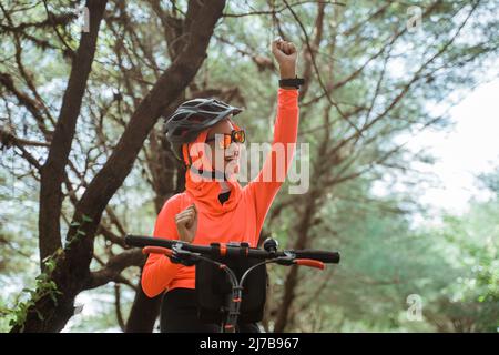 une femme excitée se levant les mains tout en pédalant sur fond d'arbres Banque D'Images