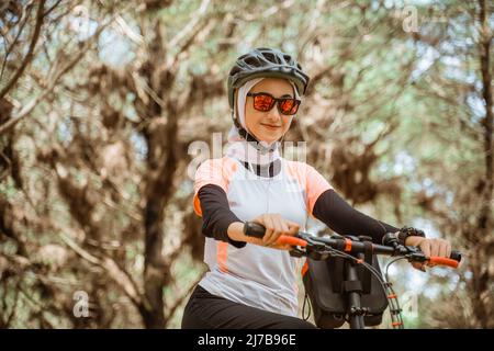 jolie fille voilée dans des lunettes de soleil souriant tout en faisant du vélo Banque D'Images