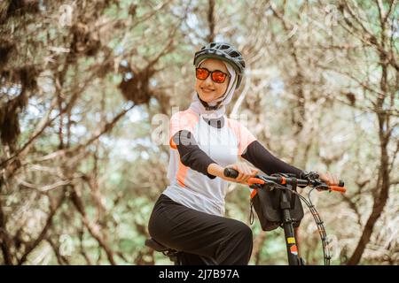 une fille voilée dans des lunettes de soleil souriant tout en faisant du vélo dans le parc Banque D'Images