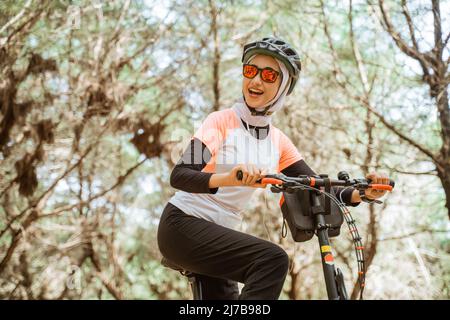 jolie fille asiatique voilée dans des lunettes de soleil portant des écouteurs vélo Banque D'Images