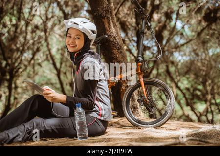 fille voilée assis au repos vélo portant des écouteurs et utilisant la tablette Banque D'Images