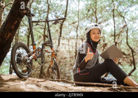 une fille voilée assise avec des écouteurs avec les pouces vers le haut pendant le vélo Banque D'Images