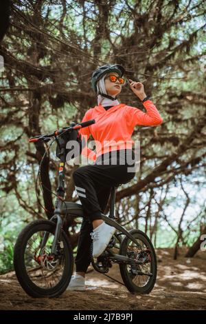 belle femme en lunettes de soleil vélo avec des arbres en arrière-plan Banque D'Images