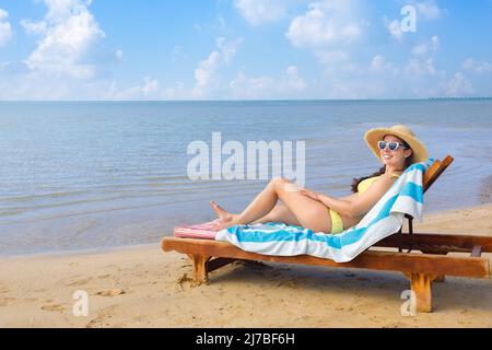 jeune femme en chapeau de paille et lunettes de soleil se détendant sur un transat Banque D'Images