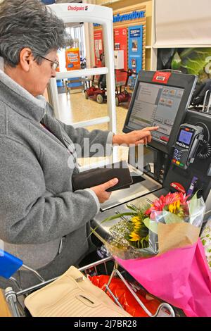 Femme tenant le sac à main shopping Tesco en libre-service vérifier que vous faites des achats jusqu'à payer par carte de débit à côté du chariot hebdomadaire complet de magasin d'alimentation Angleterre Royaume-Uni Banque D'Images