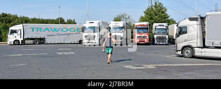 Le conducteur de camion se promette tôt le matin vers les véhicules articulés hgv garés dans les aires de stationnement de nuit de la station-service d'autoroute Angleterre Royaume-Uni Banque D'Images