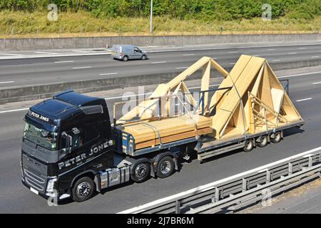 Vue latérale et avant aérienne entrepreneur de transport noir affaires camion hgv charge de remorque de chargeur bas de la remorque de construction de treillis de toit bois conduisant la route du Royaume-Uni Banque D'Images