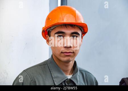 Ust'-Kamenogorsk, Kazakhstan - 31 mai 2012 : portrait d'un jeune travailleur asiatique en casque orange. Regarde directement dans l'appareil photo. Banque D'Images