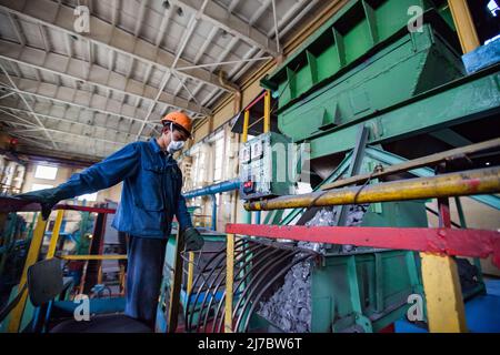 Ust'-Kamenogorsk, Kazakhstan - 31 mai 2012 : un jeune travailleur asiatique en vêtements de travail bleus et casque de sécurité orange travaille sur un convoyeur de minerai de titane. Trémie verte Banque D'Images