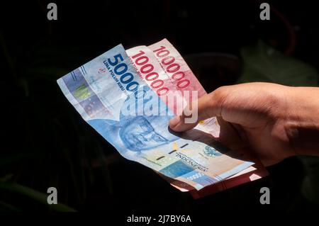 Un enfant asiatique tient l'argent indonésien dans un foyer peu profond. Concept d'enregistrement et de don Banque D'Images