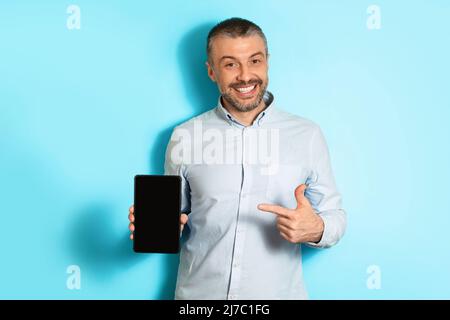 Homme d'âge moyen montrant la tablette numérique écran vide, fond bleu Banque D'Images