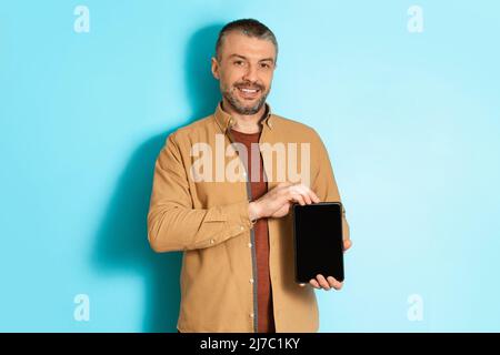 Un freelancer masculin montre une tablette avec écran vide sur fond bleu Banque D'Images