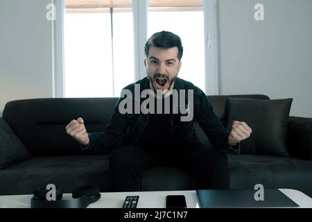 Frénésie, le jeune homme qui est très heureux que son équipe préférée a gagné le match, il se serre les mains et pleure pour la joie, le fan loyal et l'adulte heureux Banque D'Images