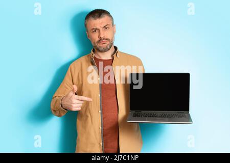 Homme d'âge moyen discontent montrant un ordinateur portable écran vide, arrière-plan bleu Banque D'Images