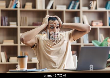 Homme arabe choqué regardant un ordinateur portable et se touchant la tête, lisant des nouvelles choquantes en ligne, assis sur le lieu de travail à la maison Banque D'Images