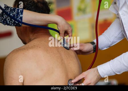 Un medic et un medic résident de sexe féminin vérifient la santé d'un patient de sexe masculin. Banque D'Images