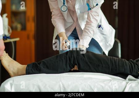 Détails avec les mains d'une jeune femme medic testant les réflexes du genou d'un patient. Banque D'Images