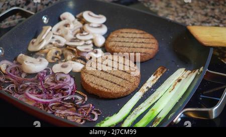 Hamburger de légumes dans une poêle en fonte avec oignons, champignons et asperges. Cuisson de la nourriture, fumée sortant de la poêle. Banque D'Images