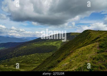 Immense nuage gris dominant une colline verdoyante dans les montagnes pendant la journée. Vue panoramique de couvert avec des buissons et des arbres de montagne pentes, sous le ciel bleu avec des cumulus nuages. Concept de haute terre. Banque D'Images