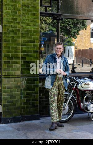 Homme élégant portant un pantalon camouflage sur le côté du pub avec une moto classique Banque D'Images