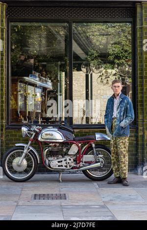 Homme élégant portant un pantalon camouflage sur le côté du pub avec une moto classique Banque D'Images