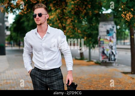 Jeune homme d'affaires portant des lunettes de soleil tout en se tenant debout à l'extérieur dans la rue. Banque D'Images