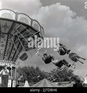 1969, historique, enfants et adultes assis dans des sièges au-dessus du sol lors d'un tour de foire, connu comme un tour de balancement ou de balancement de chaise, Angleterre, Royaume-Uni. Dans certaines parties du monde, ils sont également connus sous le nom de « promenades en chaise ou en avion ». Banque D'Images