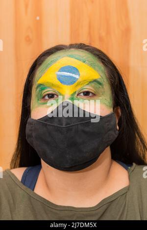 Femme avec le drapeau du Brésil peint sur son visage avec un masque noir à Rio de Janeiro. Banque D'Images