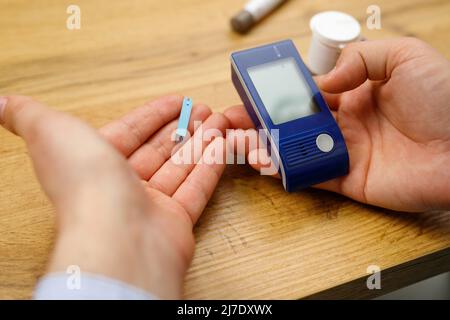 Homme mains sur la table tenant glucomètre et bandes pour vérifier le taux de sucre dans le sang, concept de diabète. Banque D'Images