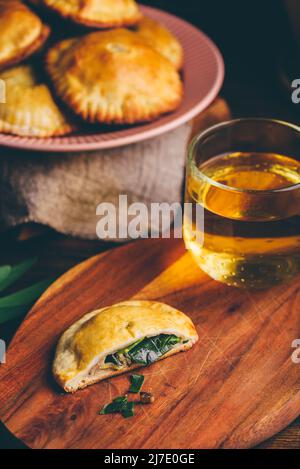 Tartes aux mains fraîchement cuites remplies de ciboulette bleue et de champignons avec une tasse de thé vert sur un plateau en bois Banque D'Images