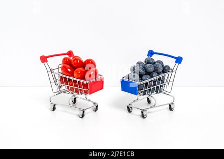 Bleuets et tomates cerises ou roms dans des chariots isolés sur fond blanc. Acheter des baies, une alimentation saine et des aliments naturels en vitamines Banque D'Images