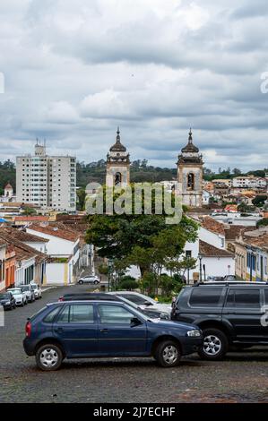 Vue sud-est de la place Largo das Merces avec des voitures garées et le paysage urbain de Sao Joao del Rei à l'arrière avec l'église Nossa Senhora do Pilar au milieu. Banque D'Images