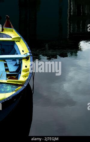 Bateau à rames en bois bleu et jaune sur l'eau reflétant le ciel - ancien bateau à rames avec un reflet de l'eau Banque D'Images