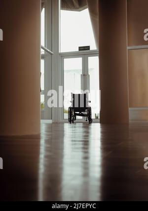 L'arrière d'un fauteuil roulant vide sans personne assis comme si vous regardiez dehors par une porte en verre. Près de la porte vitrée de sortie avec une vue extérieure floue o Banque D'Images