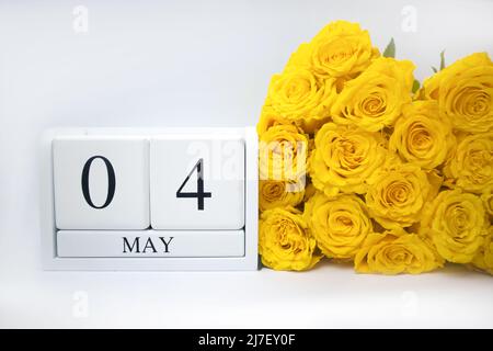 Mai 4 sur un calendrier blanc en bois et un bouquet jaune de roses sont côte à côte Banque D'Images