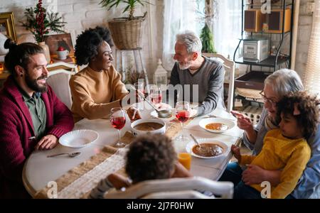 Bonne famille multiethnique multigénération s'amusant autour d'une table de cuisine. Banque D'Images