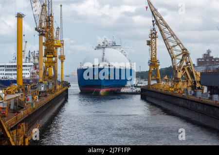 Transporteur de GNL arrivant dans un chantier de réparation de navires assisté par plusieurs remorqueurs. Le quai flottant est immergé pour permettre l'entrée du bateau. Banque D'Images