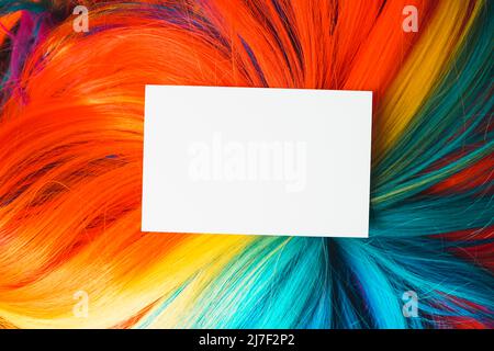Maquette d'une carte blanche de très près sur une perruque arc-en-ciel colorée et multicolore avec beaucoup de texture de cheveux Banque D'Images