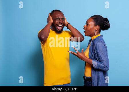 Une femme hurle devant un homme qui couvrait ses oreilles pour arrêter de s'exprimer, exprimant ainsi sa frustration. Couple malheureux se battant et criant en studio, ayant des problèmes de relation. Bouleverser les personnes en conflit. Banque D'Images