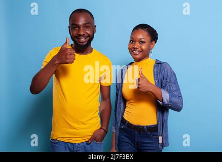 Partenaires optimistes montrant un bon signe d'accord, se tenant sur fond bleu. Homme positif et femme faisant un geste correct avec les mains, se sentant confiant dans le choix réussi. Banque D'Images