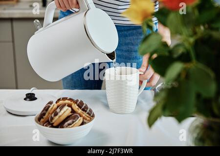 Temps du thé, femme versant de l'eau bouillie de la bouilloire électrique dans la tasse pour préparer le thé, petit déjeuner dans la cuisine Banque D'Images