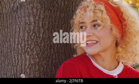 Jeune femme caucasienne attrayante debout près de l'arbre dans le parc, regardant loin et souriant de l'espace de copie de gros plan. Photo de haute qualité Banque D'Images