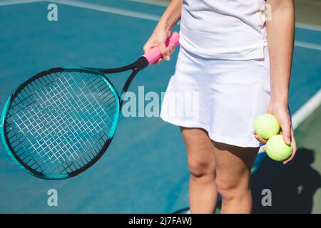 Mi-section de jeunes femmes caucasiennes tenant des balles de tennis et raquette sur le terrain par temps ensoleillé Banque D'Images