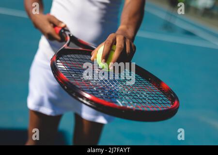 Section médiane d'une joueuse afro-américaine tenant le ballon sur l'ouverture sur le court de tennis par beau temps Banque D'Images