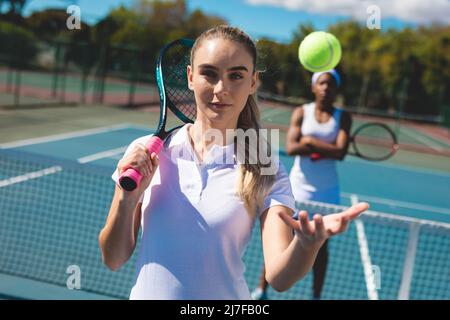 Portrait d'une joueuse de tennis caucasienne confiante qui a pris le ballon avec un concurrent afro-américain Banque D'Images