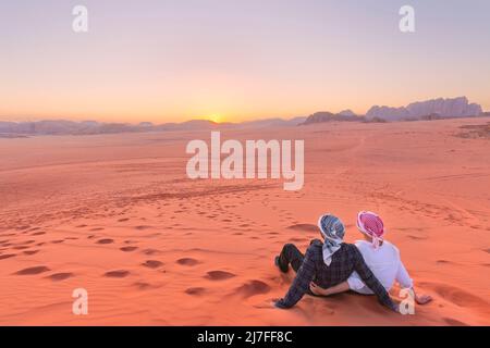 Un jeune couple regarde au lever du soleil sur le rhum wadi Désert en Jordanie Banque D'Images