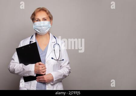 Médecin senior femme en masque médical et manteau blanc avec stéthoscope Banque D'Images