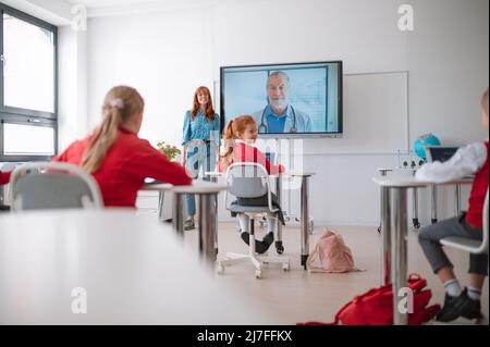 Vue arrière d'un groupe d'enfants assis et à l'écoute d'un enseignant en classe Banque D'Images