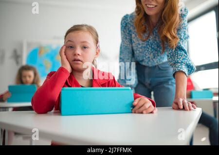 Down syndrome écolière utilisant la tablette avec l'aide de l'enseignant pendant la classe à l'école, concept d'intégration. Banque D'Images