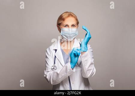 Portrait d'une femme médecin attirante, portant un manteau blanc et des gants bleus Banque D'Images